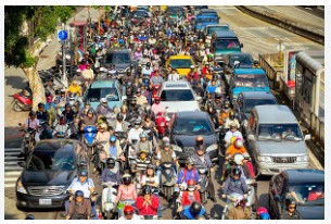 An image showing a busy road scene with cyclists, pedestrians, and motorcyclists in an urban setting